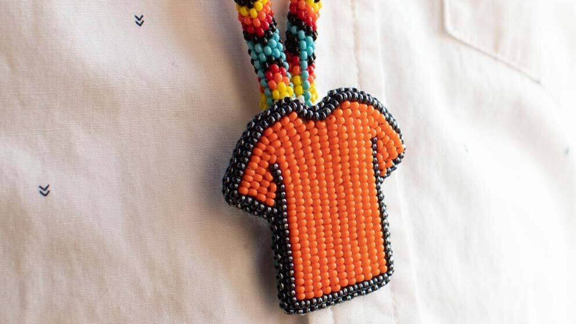 Image shows an orange t-shirt keychain that a person (face not shown) is wearing.