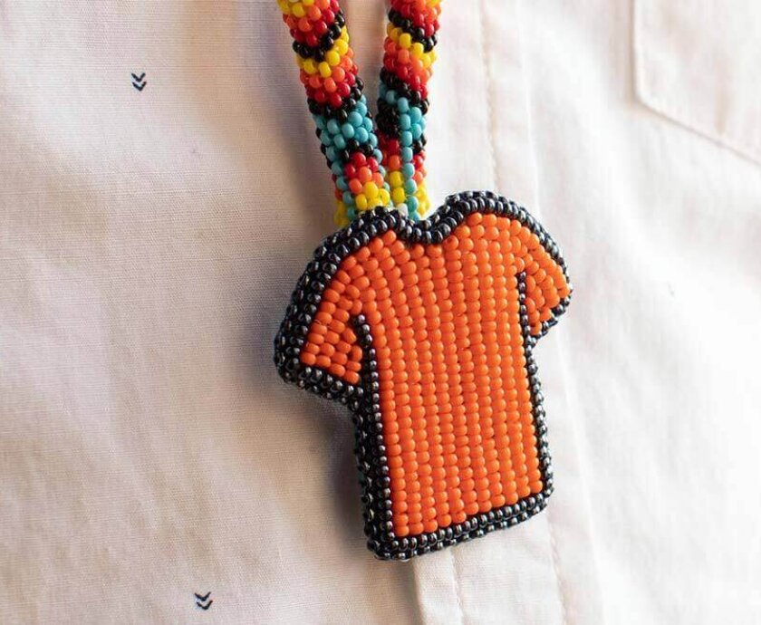 Image shows an orange t-shirt keychain that a person (face not shown) is wearing.